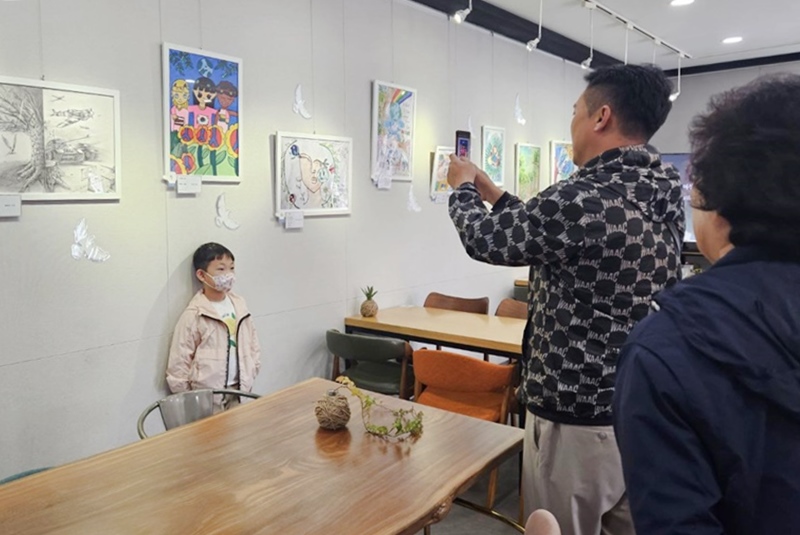 한 가족이 전시된 어린이의 작품을 배경으로 스마트폰에 담아내고 있다.